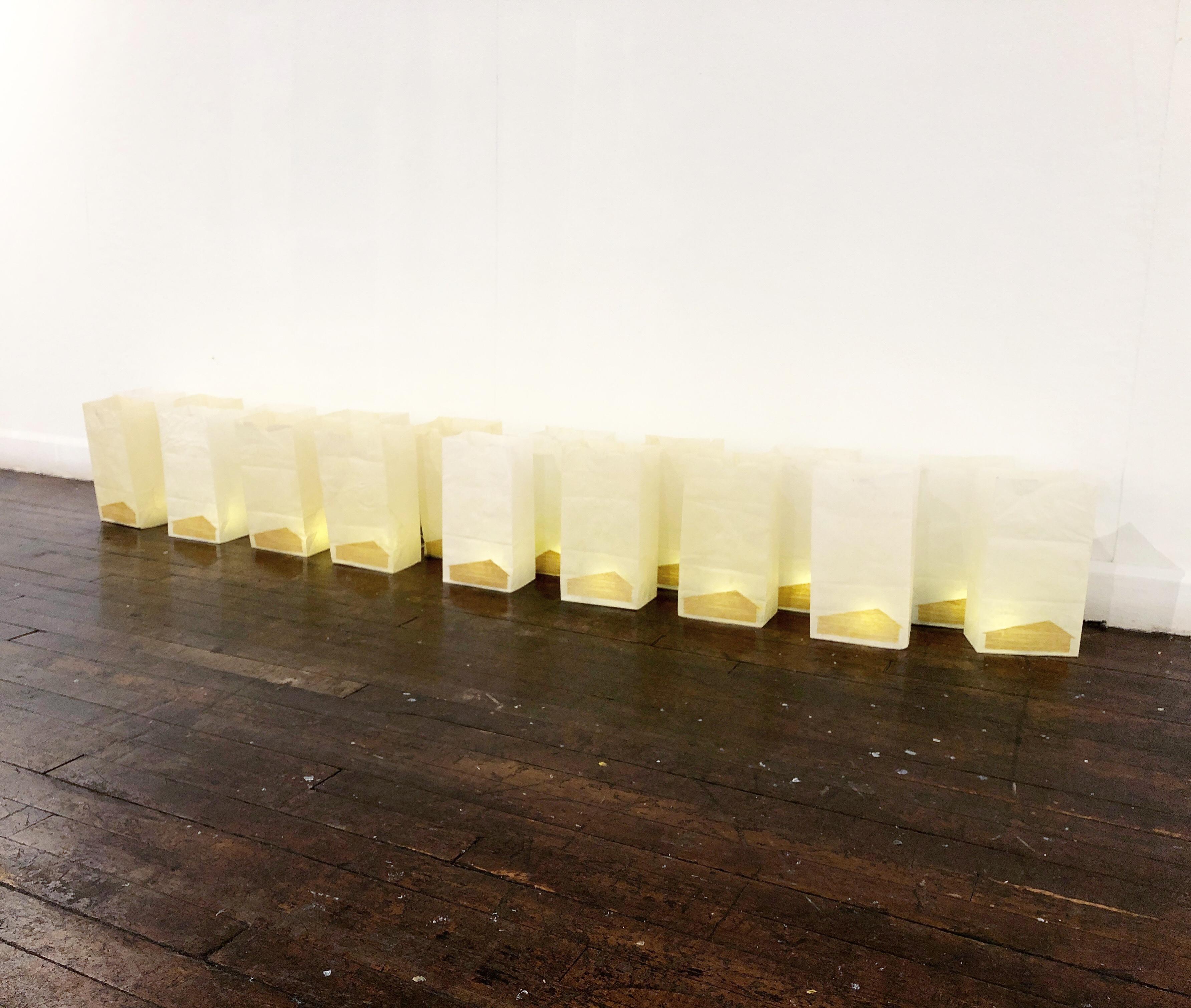 A vigil for the victims of the forest fire that destroyed Paradise, California. Each paper bag is dipped in beeswax, and has lit with an electric candle. Each bag is adorned with a silhouette of a simple mid-century ranch home, typical of the town. 